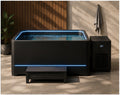 A modern black outdoor hot tub with blue LED lighting and a matching black circulation unit, shown in a styled patio setting with a bench, tiled floor, wood slat wall, and a towel hanging on a hook.